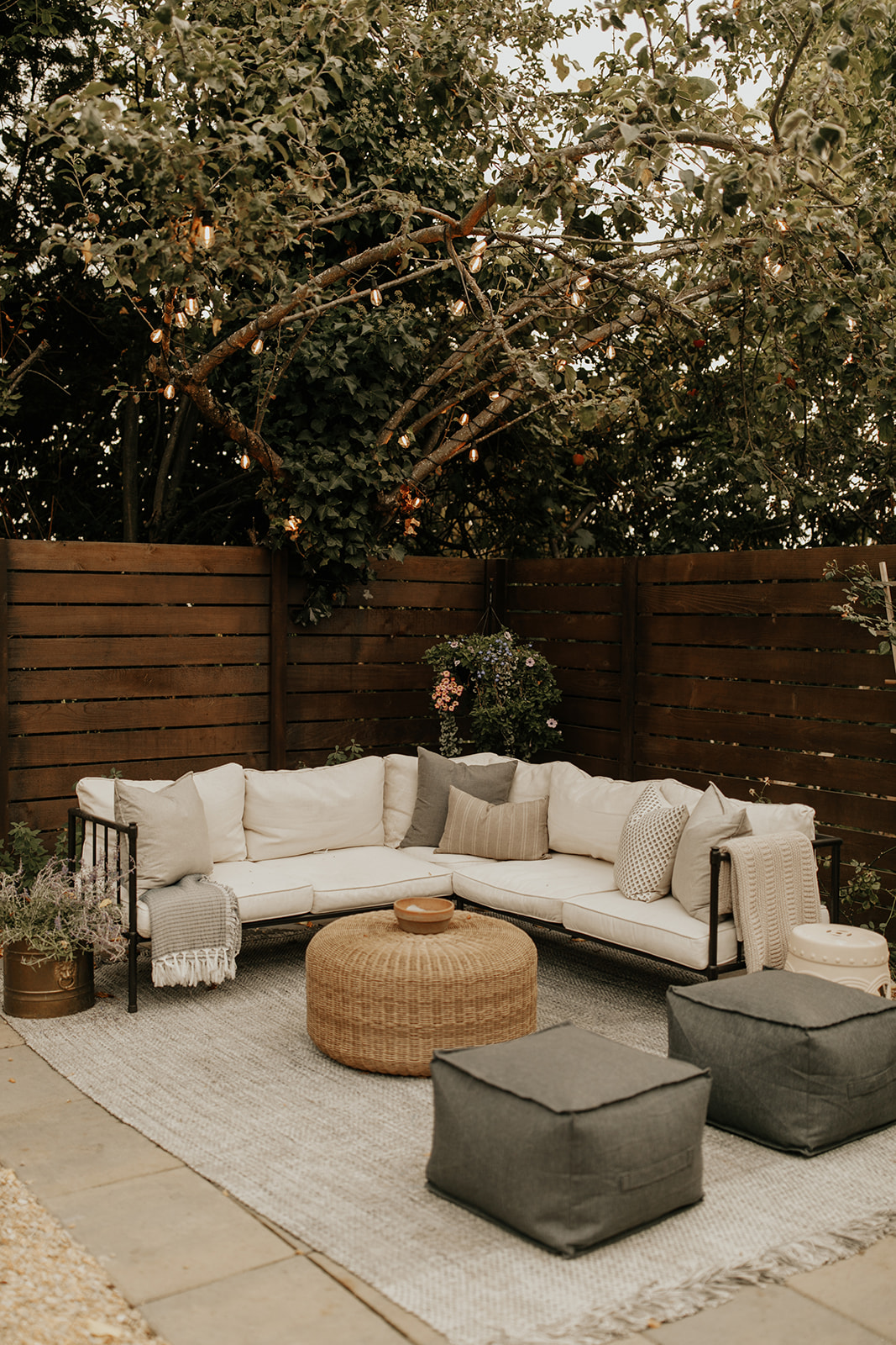 A backyard patio with an outdoor rug, couch with pillows, coffee table and string lights in the tree above