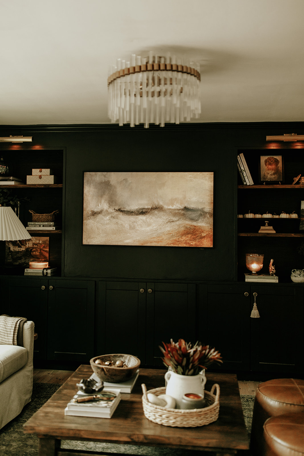 A Samsung Frame TV is mounted on a wall in between built in cabinets that are recessed. In front of the cabinet wall is a well decorated coffee table and cozy couch.