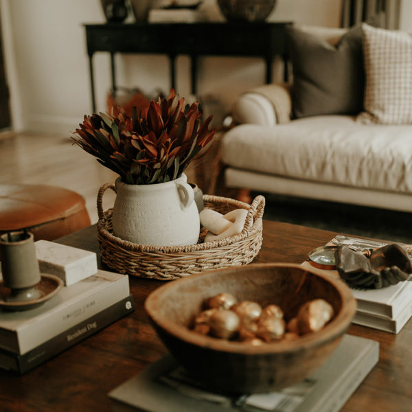 A coffee table sits in a living room, decorated with coffee table books, flowers, and vintage décor items