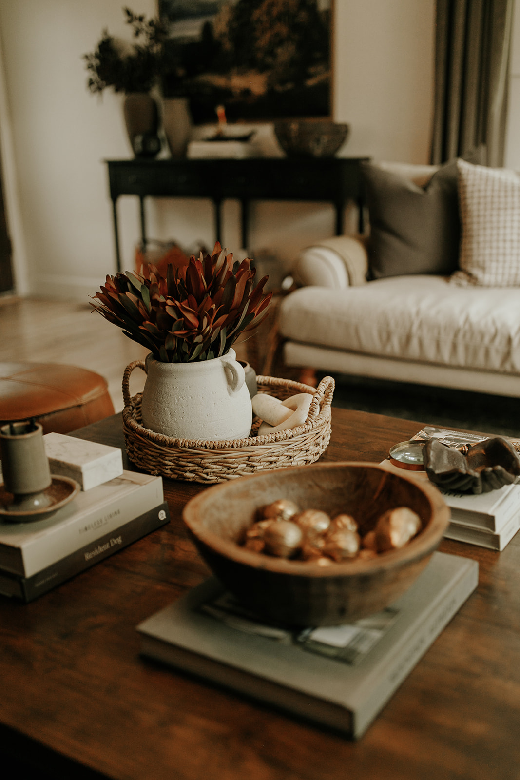 A coffee table sits in a living room, decorated with coffee table books, flowers, and vintage décor items